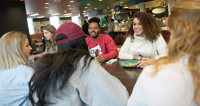 一群学生在沃特森餐饮中心的一张桌子边聊天边吃饭.